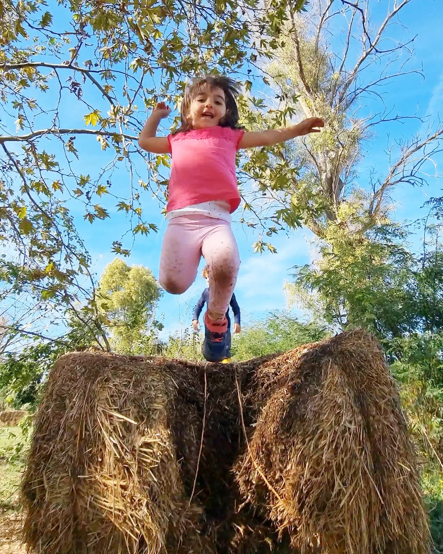 Bambina salta gioiosa da una balla di fieno