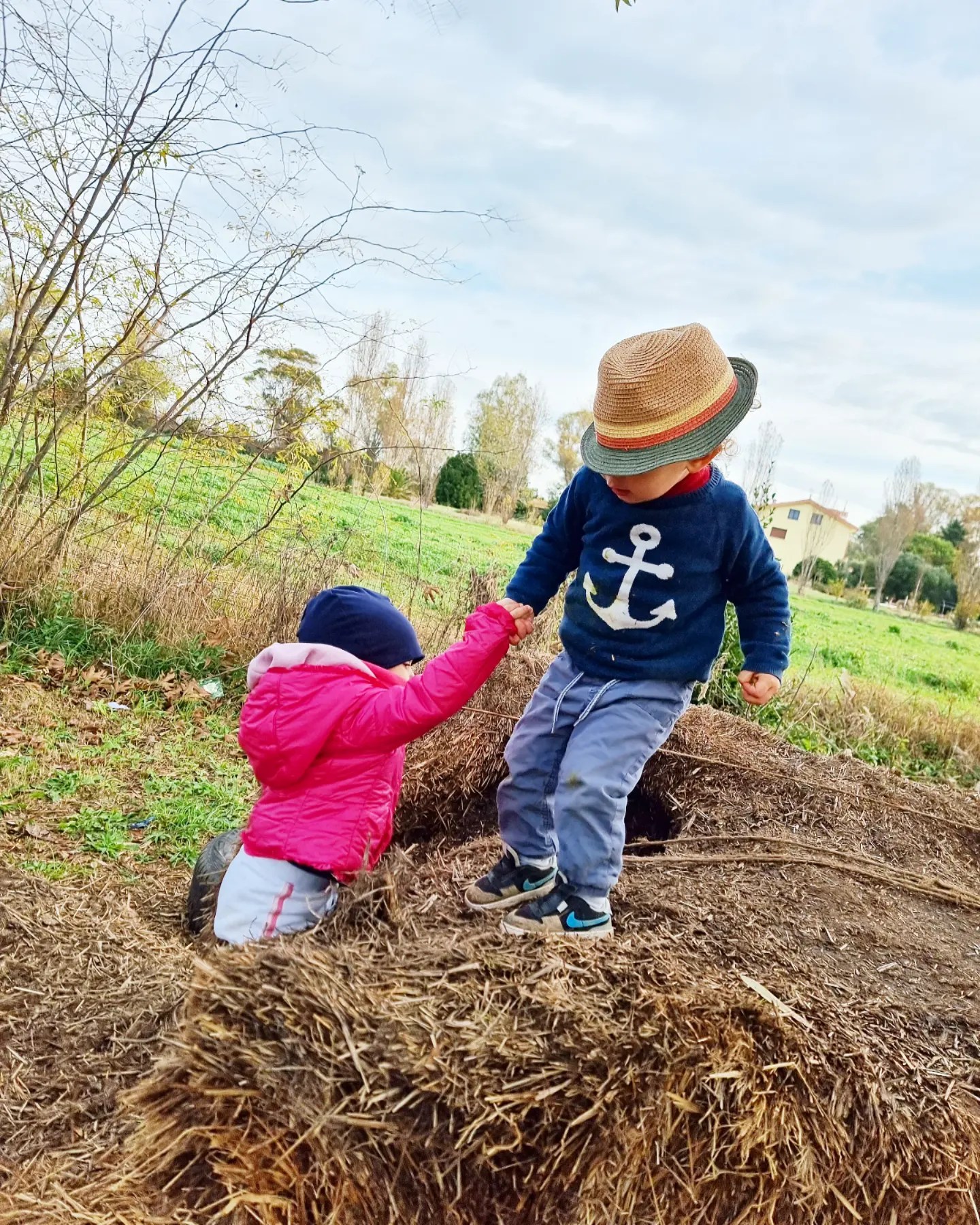 Bambino aiuta un'altra bambina a salire su una balla di fieno