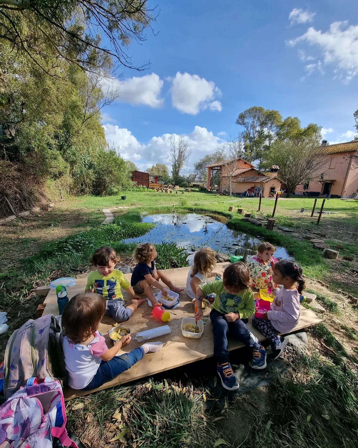 Bambini pranzano insieme accanto a uno stagno in un giardino naturale